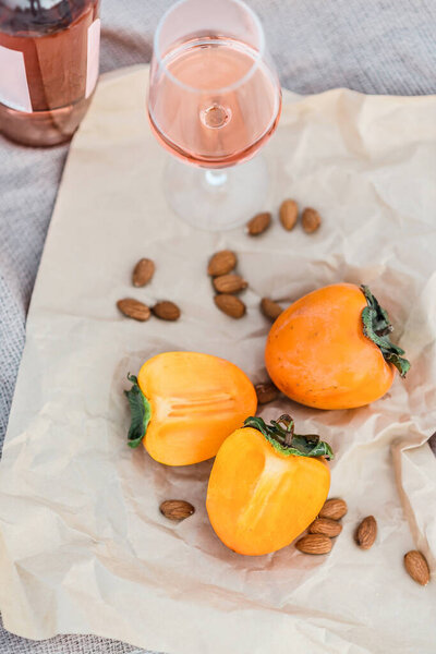 Picnic on the beach with persimmons, almond and bottle of rose wine on beige blanket.