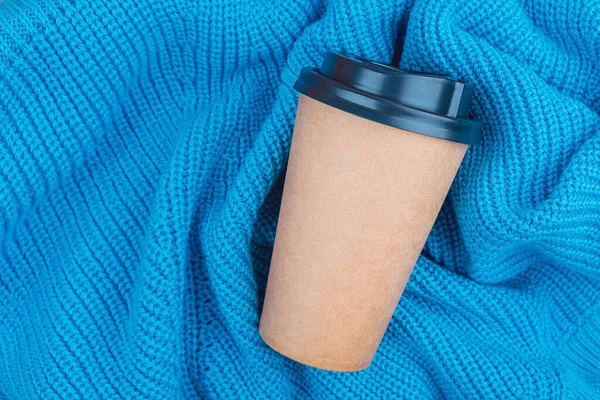 Coffee paper cup on knitted blue blanket background, top view flat lay. Take away coffee cup.