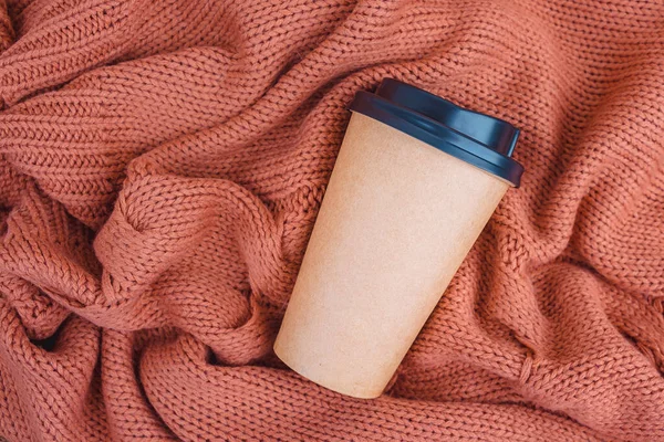 Kaffeepapiertasse auf orangefarbener Strickdecke Hintergrund, Draufsicht flach liegend. Kaffeetasse zum Mitnehmen. Stockbild