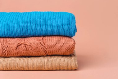 Turuncu, mavi ve bej renkli turuncu arka planda katlanmış sıcak örülmüş kadın süveteri yığını..