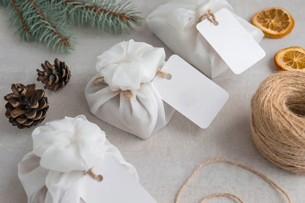 Weihnachtsgeschenke umhüllt mit weißem Furoshiki-Stoff, Etiketten und getrockneten Orangenscheiben. umweltfreundliches Geschenk. Stockbild