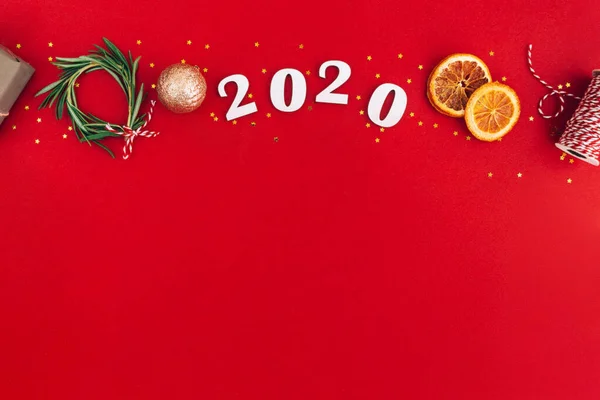 Χριστουγεννιάτικο χειροποίητο οβάλ πλαίσιο από ξύλινα νούμερα 2020 και κλαδιά ελάτης και άλλα χριστουγεννιάτικα στολίδια σε κόκκινο φόντο. — Φωτογραφία Αρχείου