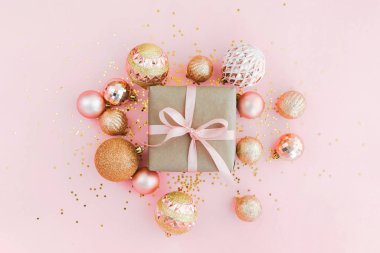 El işi kağıdına sarılı hediye kutusu soluk pembe arka planda pembe kurdele parıltılı ve altın Noel ağacı topları.