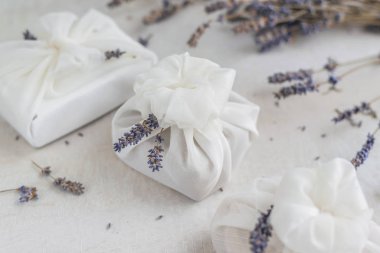 Beyaz furoshiki kumaşıyla sarılmış ve lavanta çiçekleriyle süslenmiş bir hediye. Çevre dostu hediye..