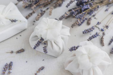 Beyaz furoshiki kumaşıyla sarılmış ve lavanta çiçekleriyle süslenmiş bir hediye. Çevre dostu hediye..
