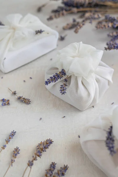 Geschenk mit weißem Furoshiki-Stoff umwickelt und mit Lavendelblüten verziert. umweltfreundliches Geschenk. lizenzfreie Stockfotos