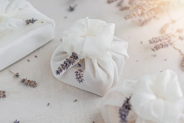 Geschenk mit weißem Furoshiki-Stoff umwickelt und mit Lavendelblüten verziert. umweltfreundliches Geschenk. — Stockfoto
