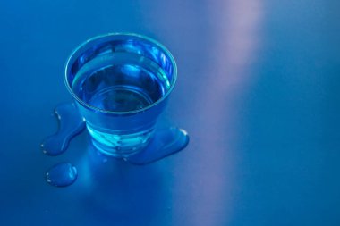 Mavi neon arka planda üzerine su dökülmüş mavi bardak..