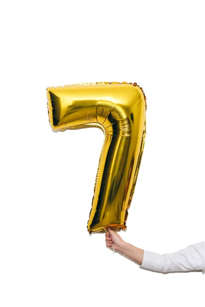 Dětská ruka se zlatým balónem číslo sedm, 7 izolovaných na bílém pozadí. — Stock fotografie