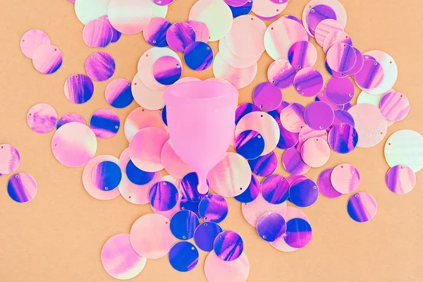 Menstruationstasse mit holografischen Pailletten, die die Menstruation auf pastellorangefarbenem Hintergrund symbolisieren. — Stockfoto