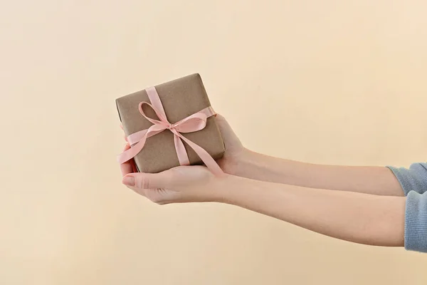 Feminino mão segurando caixa de presente envolto em papel artesanal com fita rosa através de fundo bege pálido . — Fotografia de Stock