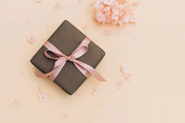 Caja de regalo envuelta en papel artesanal con cinta rosa sobre fondo naranja pálido con flores de hortensias . — Foto de Stock