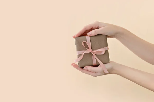 女性手持礼品盒，用粉红缎带包裹在浅褐色背景的工艺用纸中. 免版税图库图片