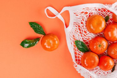 Turuncu arka planda yeşil yapraklı taze mandalinalar. Düz yatış, üst görünüm.