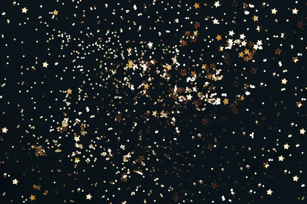 Coriandoli di glitter stellati dorati su sfondo nero scuro. Sfondo festivo di vacanza. Concetto di celebrazione . — Foto Stock