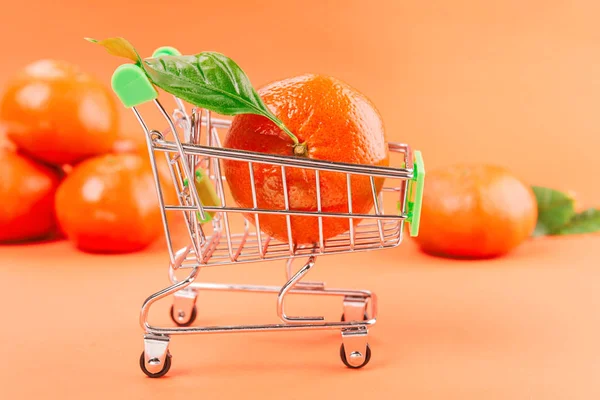 Toy shopping cart with many mandarins on orange background. — 스톡 사진