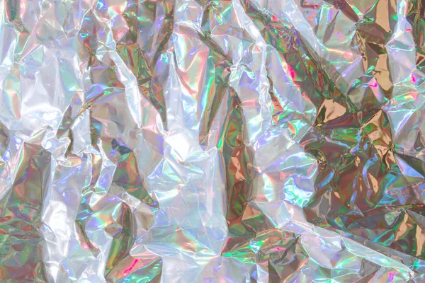 Crumpled holographic wrapping paper with shiny effect. Close up, top view. Creative texture.