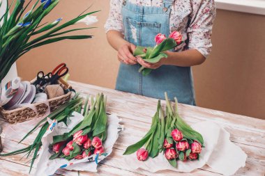 Genç bayan çiçekçi taze çiçeklerle çalışıyor. Masada zambak buketi yapıyor..