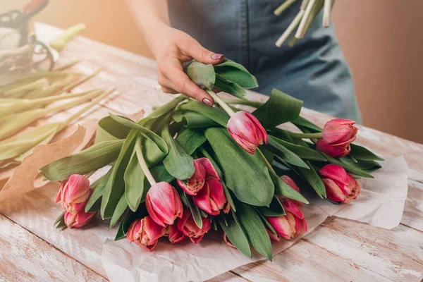 Hände einer jungen Floristin, die mit frischen Blumen arbeitet und einen Strauß rosa Rosen auf den Tisch stellt. lizenzfreie Stockbilder