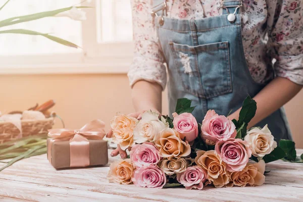 年轻女性花匠的手在桌上用鲜花做粉红色玫瑰花束 靠近点 图库照片