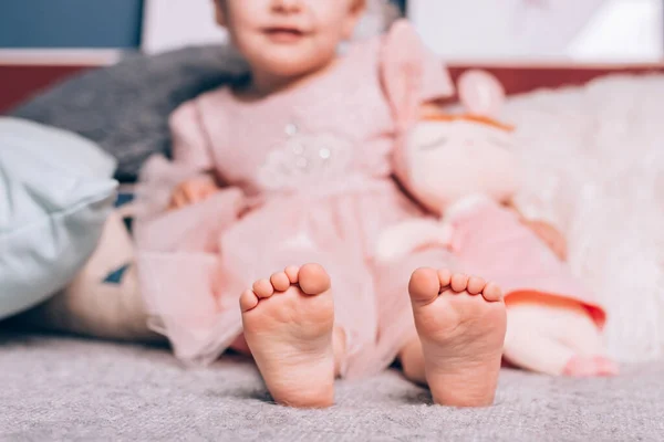 可爱的小孩赤着脚躺在温暖的针织毛毯上，还有柔软的玩具。舒适的家时间，生活方式. — 图库照片
