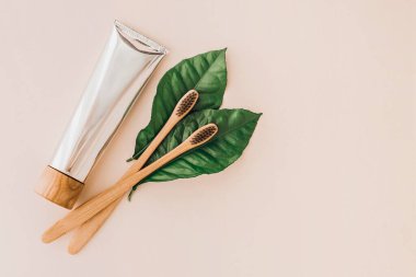 Bambu doğal diş fırçaları, diş macunu ve soluk arkaplanda taze yapraklar. Sıfır atık ve plastiksiz konsept. Sürdürülebilir yaşam tarzı kavramı.