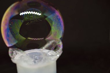 Soyutlama. Siyah arka planda suyun üzerinde sabun köpükleri. Renk oyunu. Bulanık renkli baloncuklar. Yakın plan..