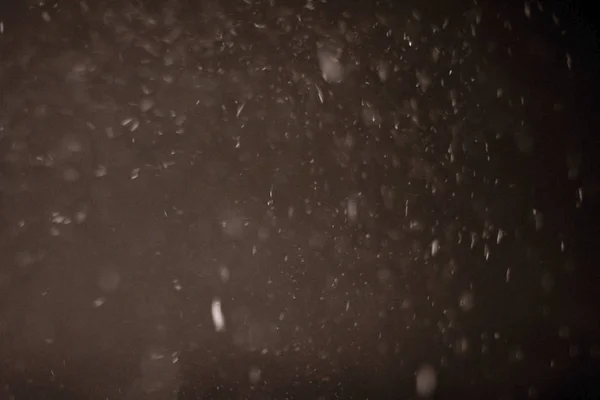 Soyut Kar, karanlık bir kış gecesinde düşer. Kar taneleri bokeh bulanık efekti.