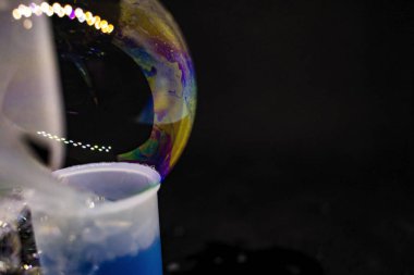 Soyutlama. Siyah arka planda suyun üzerinde sabun köpükleri. Renk oyunu. Bulanık renkli baloncuklar. Yakın plan..