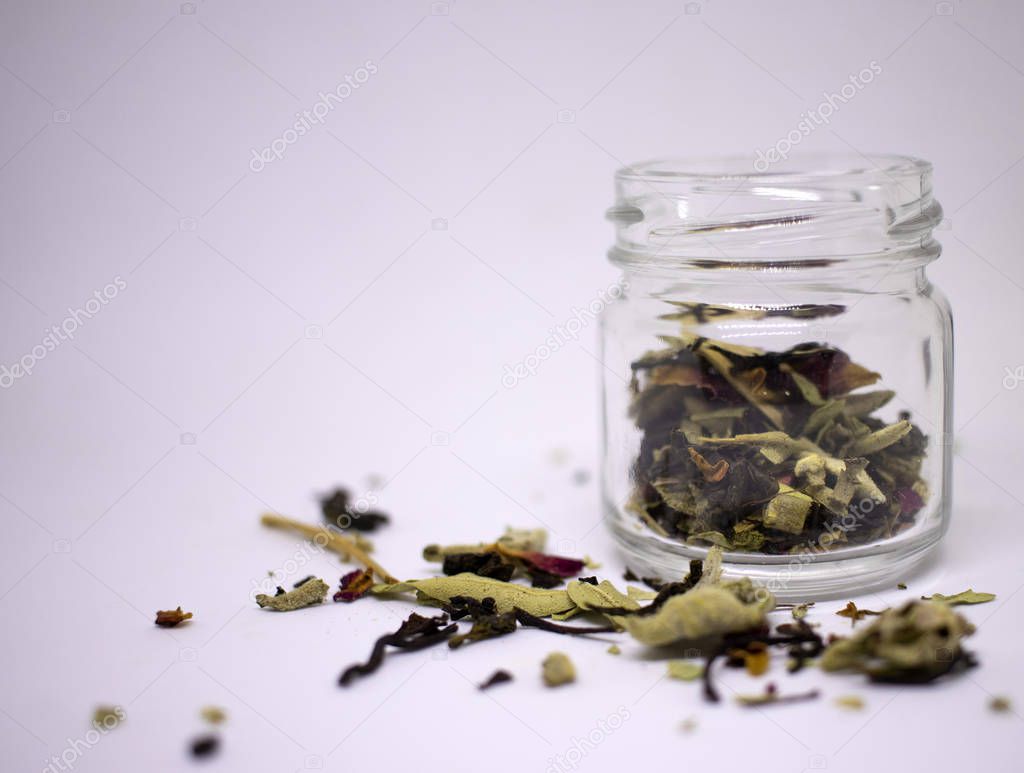 A mixture of bio herbal and flower dried tea. In a jar and in bulk on a white background. Place for text. Close-up.