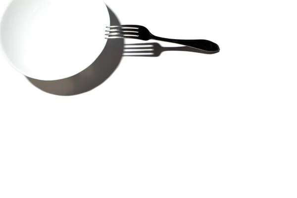 Λευκό στρογγυλό πιάτο με ένα μεταλλικό πιρούνι σε λευκό φόντο — Φωτογραφία Αρχείου