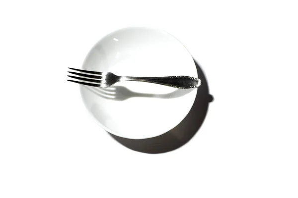 Placa redonda branca com um garfo de metal em um fundo branco — Fotografia de Stock