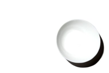 White deep plate in the lower right corner with backlight on a white background, top view with place for text. Minimalism.
