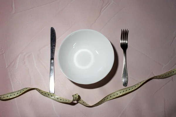 Υγιή κατανάλωση ή να κάνει δίαιτα έννοια. άδειο πιάτο, πηρούνι και μαχαίρι τυλιγμένο σε μεζούρα. — Φωτογραφία Αρχείου