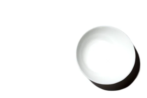 Assiette profonde blanche dans le coin inférieur droit avec rétro-éclairage sur fond blanc, vue du dessus avec place pour le texte. Minimalisme . — Photo