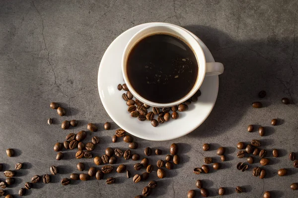 Tasse blanche avec soucoupe et grains de café, aromatique, café chaud sur une couche plate sombre — Photo