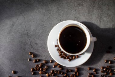 Beyaz fincan çay tabağı ve kahve çekirdekleri, aromatik, koyu bir düzlükte sıcak kahve.