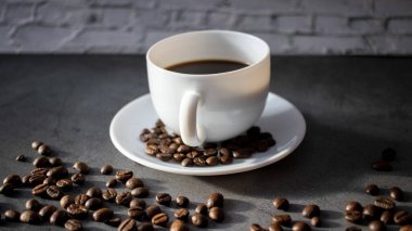 Beyaz fincan çay tabağı ve kahve çekirdekleri, aromatik, koyu bir düzlükte sıcak kahve.