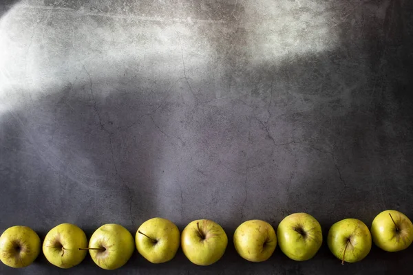 Pommes jaunes sont situés ci-dessous, une rangée de pommes sur un fond sombre avec des rayons de soleil . — Photo