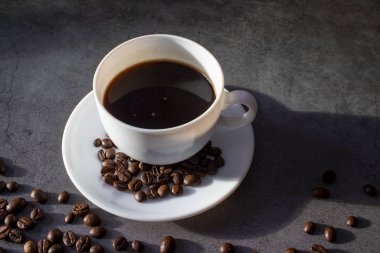 Beyaz fincan çay tabağı ve kahve çekirdekleri, aromatik, koyu bir düzlükte sıcak kahve.