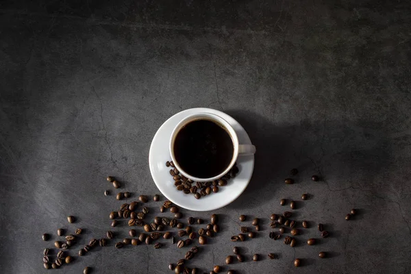 Tasse blanche avec soucoupe et grains de café, aromatique, café chaud sur une couche plate sombre — Photo