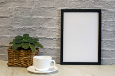 Duvarın arkasındaki siyah çerçevenin boş bir suretinin ön görüntüsü. Bir fincan kahve, çiçekler..