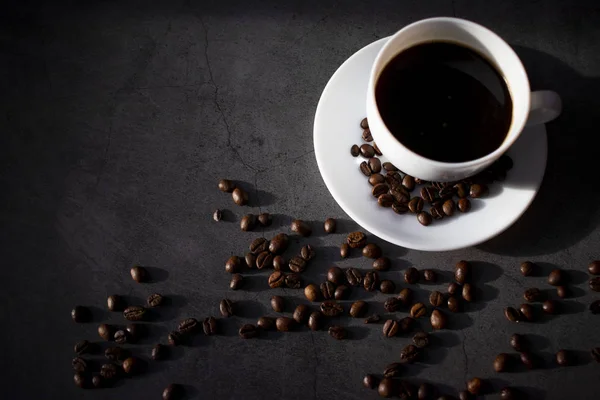 Tasse blanche avec soucoupe et grains de café, aromatique, café chaud sur une couche plate sombre — Photo