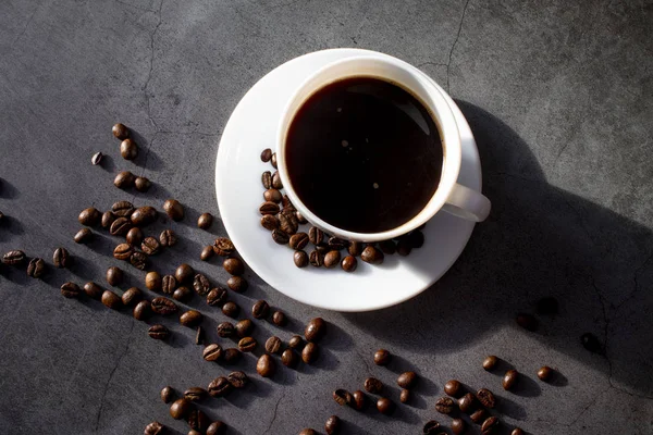 Tasse blanche avec soucoupe et grains de café, aromatique, café chaud sur une couche plate sombre — Photo