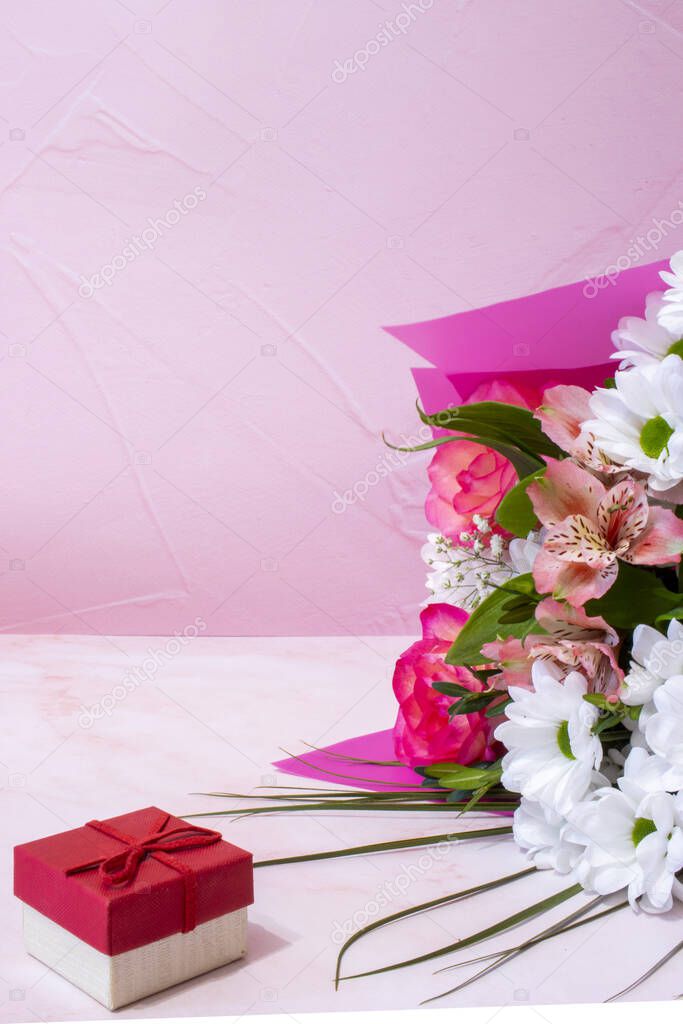 Romantic background with a bouquet of colorful flowers and a gift box on pink. Side view with copy space. Mothers Day, Womens Day background.