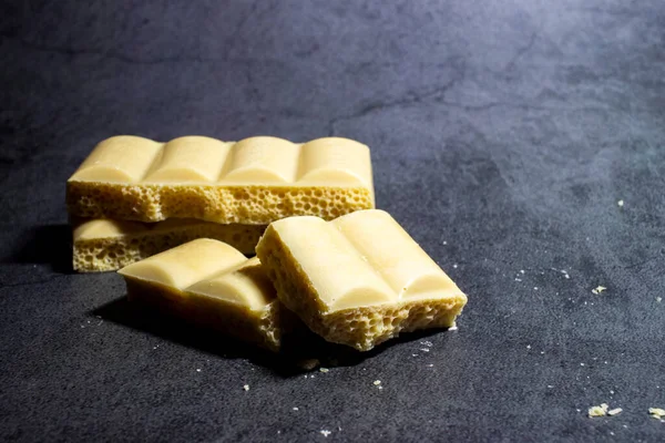 Broken bar of white chocolate on a black background. A delicious bar of milk chocolate. Selective focus