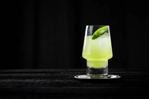 Gin Basil Smash, green cocktail on black wooden bar with black background