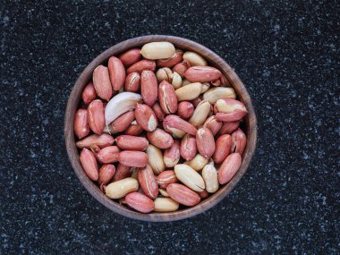 Bir kase kavrulmuş tuzsuz fıstık ve siyah mermer mutfak masasının arkasındaki ahşap kasede saklı bir diş sarımsak.