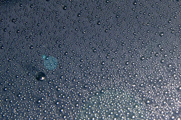 Water droplets on the glass glisten in a beam of light on a black background, close-up texture