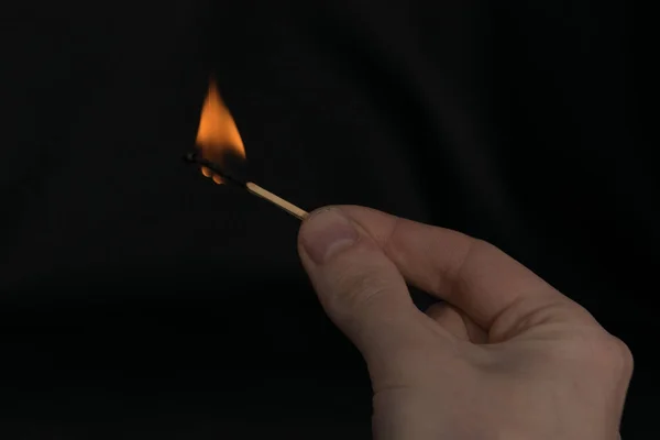 burning match in hand on black background